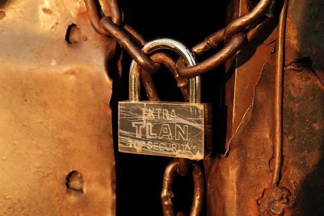 A brass-coloured padlock and heavy chain secure a rusty metal door in warm evening light.