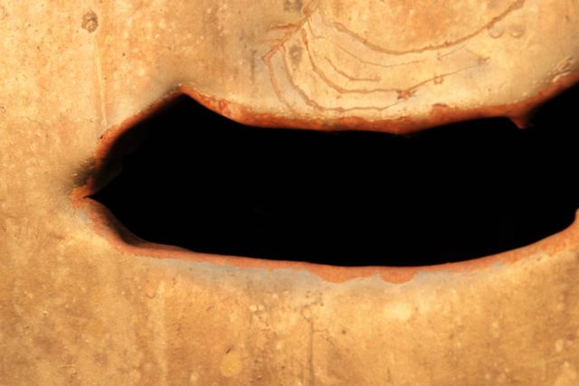 A dark opening and curved lines in a heavily rusted metal surface, lit by warm evening sun.