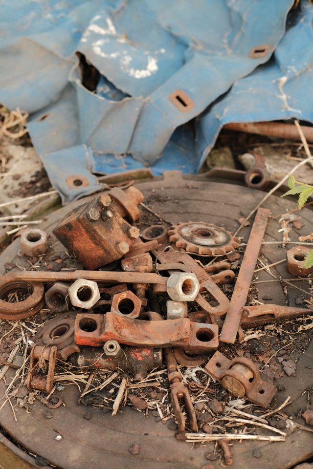 Old metal fittings and rusty tools lie on the ground beneath a folded blue tarpaulin.