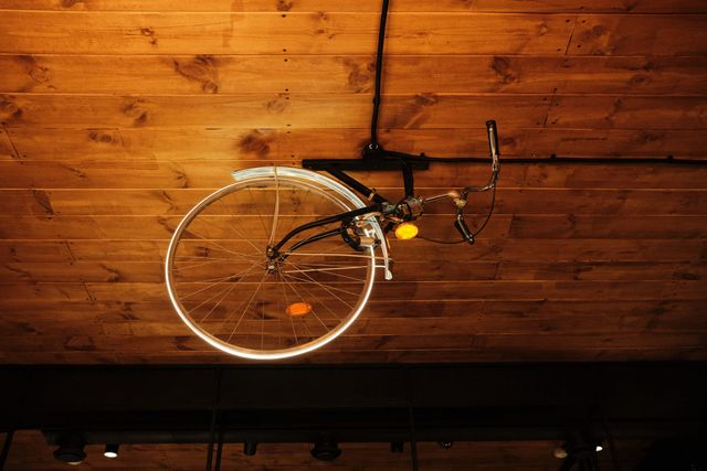 An old bicycle is mounted under a timber ceiling, its pale front wheel and curved handlebars seen from below.