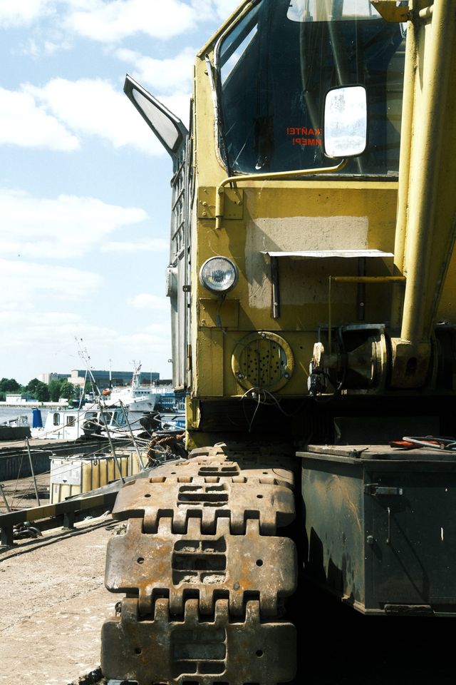 Broad steel crawler tracks lead toward the yellow cab and dark windows of an old crane.