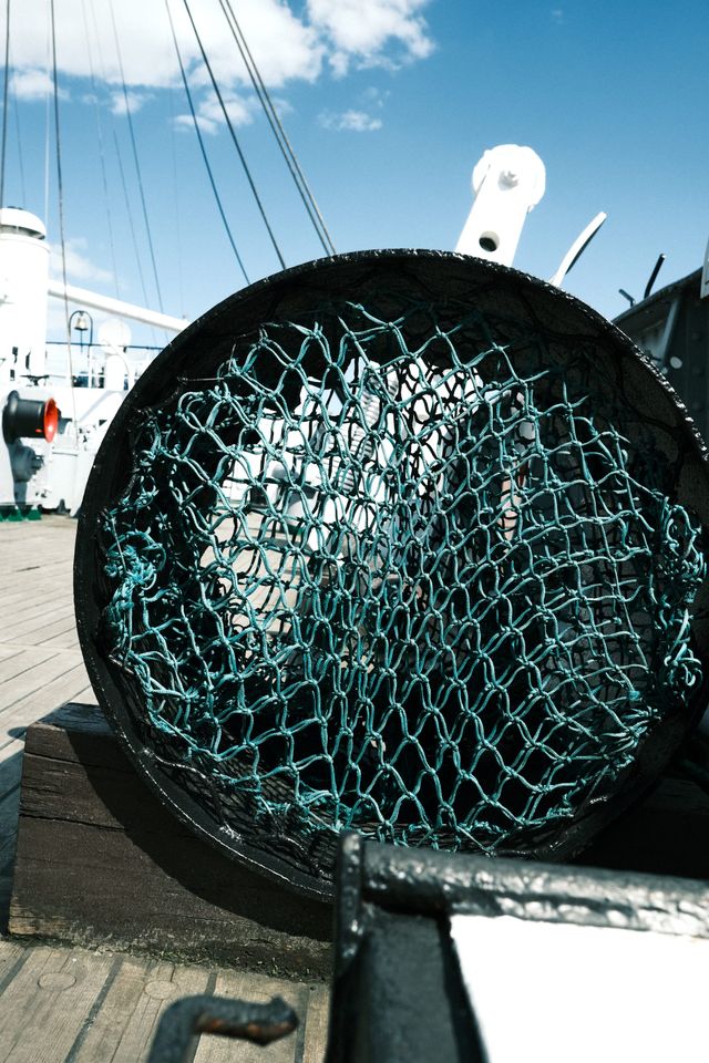 Green wire mesh covers a round black metal housing on a sunlit ship deck.
