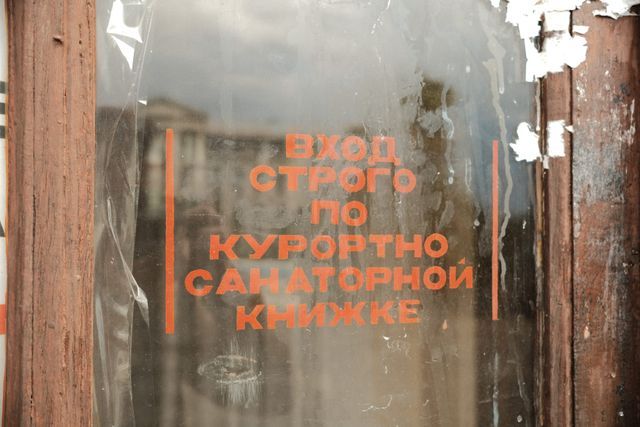 Faded orange Cyrillic lettering remains on a dark wooden-framed window of an old resort building.