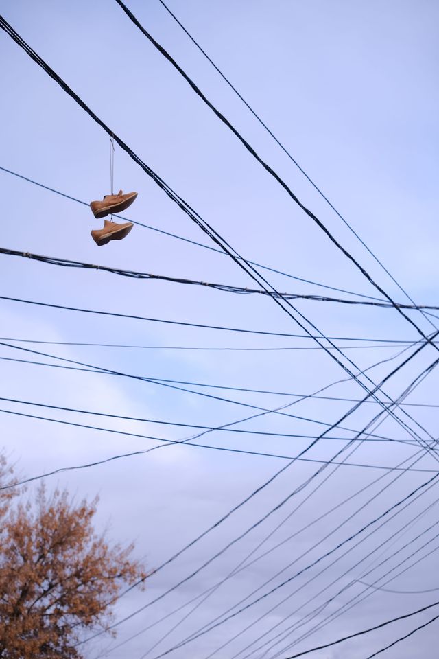 淡い空を背景に交差する電線の間で二つの靴が下がる。
