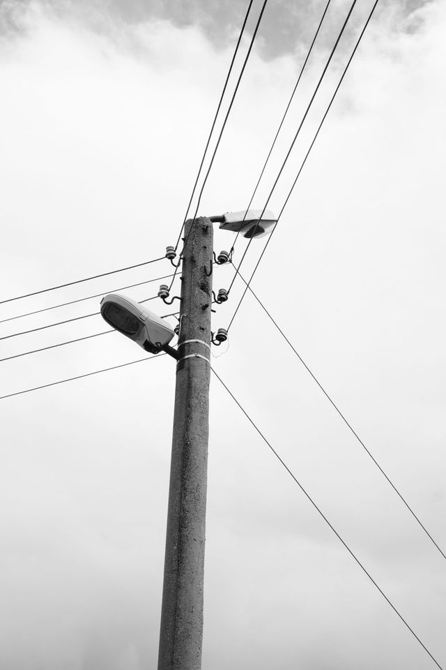 曇り空の下に曲がった街灯を備えたコンクリート電柱が立つ。