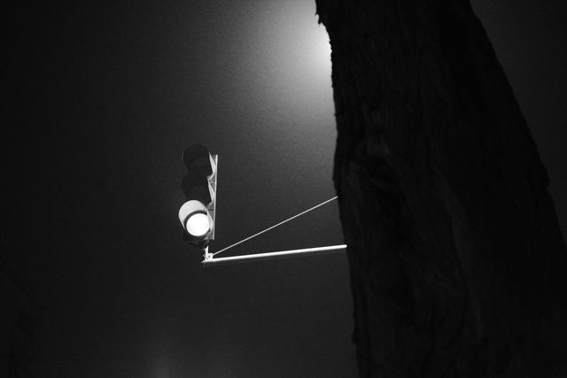 暗い建物の狭い隙間に街灯と電線が見えるモノクロ写真。
