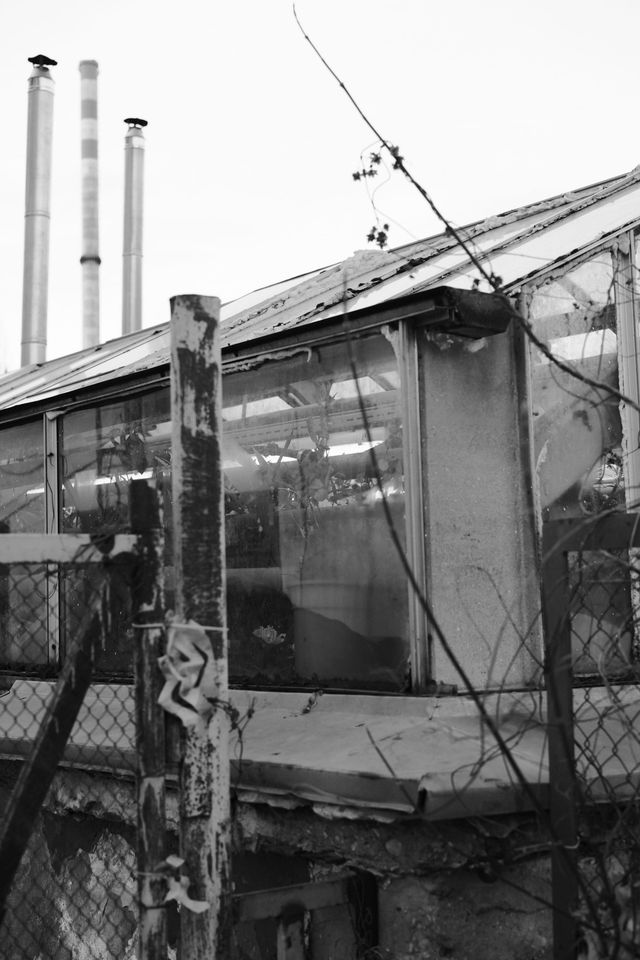 金網フェンスとケーブルの奥にある古びた小屋のモノクロ写真。